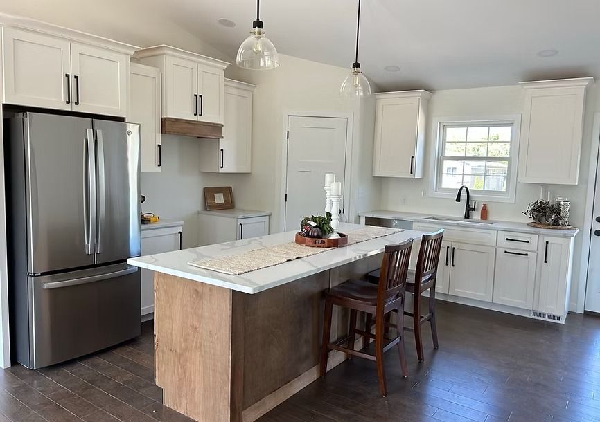 Bright kitchen with white cabinets, stainless fridge, marble island, and two wooden stools.