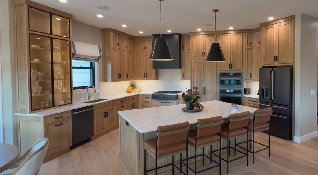 Modern kitchen with wood cabinets, white island, black pendant lights, and bar stools