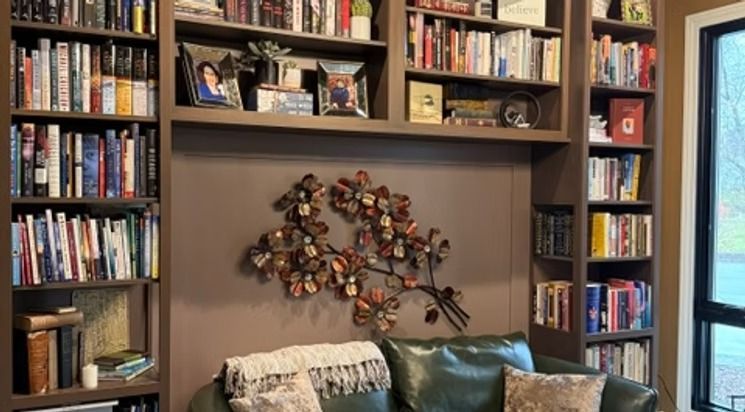 Cozy living room with tall bookshelves, a decorative wall sculpture, and a couch below a window.