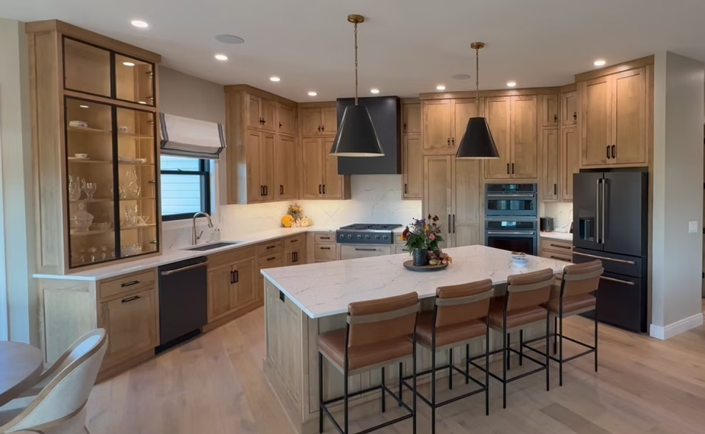 Modern kitchen with wood cabinets, large island, pendant lights, and stainless steel appliances.