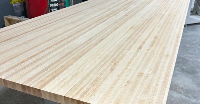 Light-colored wood tabletop board with visible grain, resting on supports in a workshop