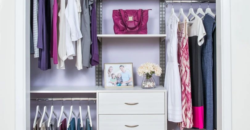 Open closet with hanging clothes, shelves, drawers, and a pink handbag in a neat dressing area