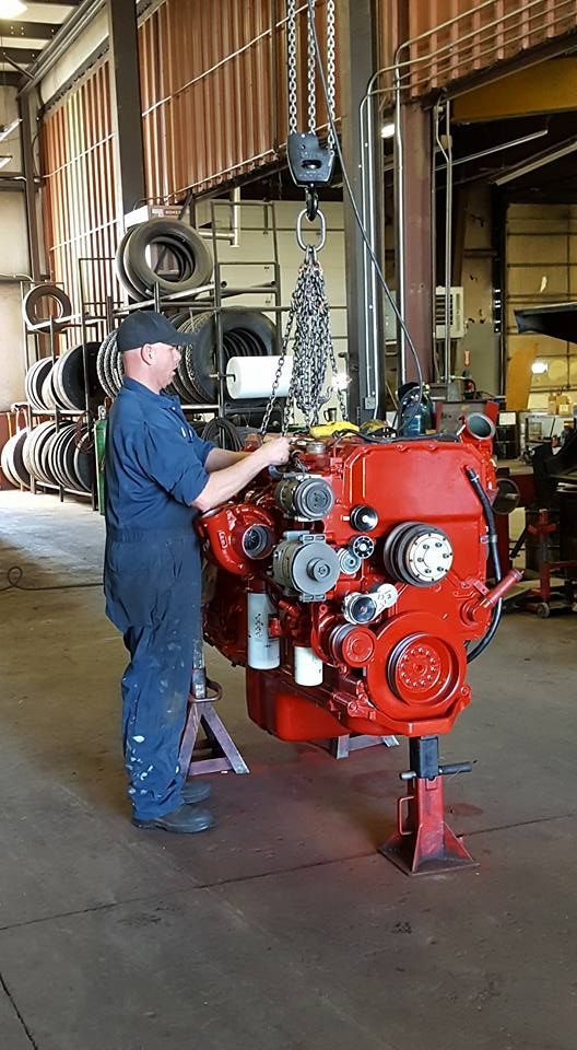Mechanic working on a red engine in an industrial workshop with hanging tires and equipment.