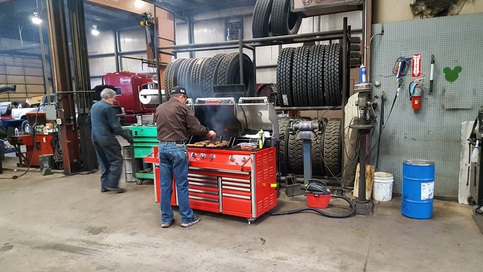Two mechanics work beside a red tool chest in an auto repair shop with stacked tires.