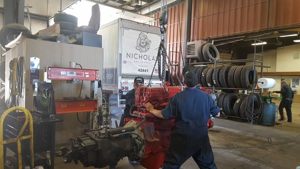 Mechanic working on heavy machinery in an industrial garage with stacked tires and equipment