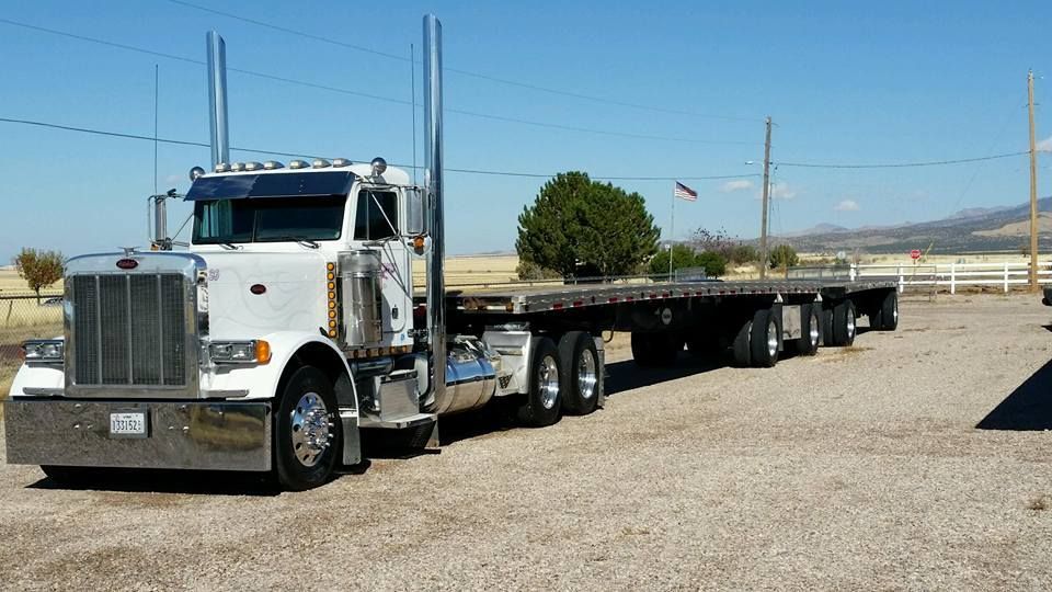 White flatbed semi truck parked on a gravel lot under a clear blue sky