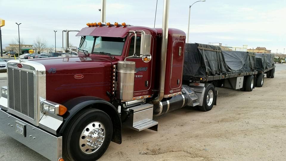 Red semi-truck with a gray covered trailer parked on a lot at dusk