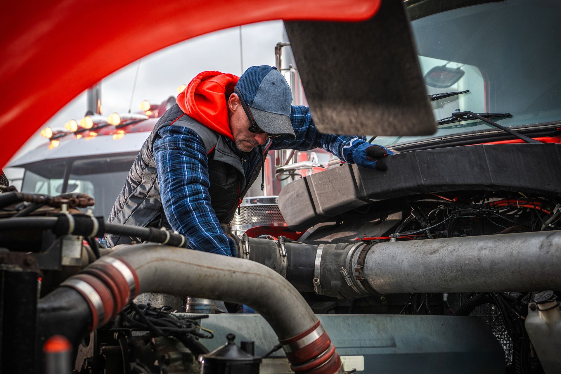 Mechanic in blue jacket inspecting engine bay of a race car under a red hood