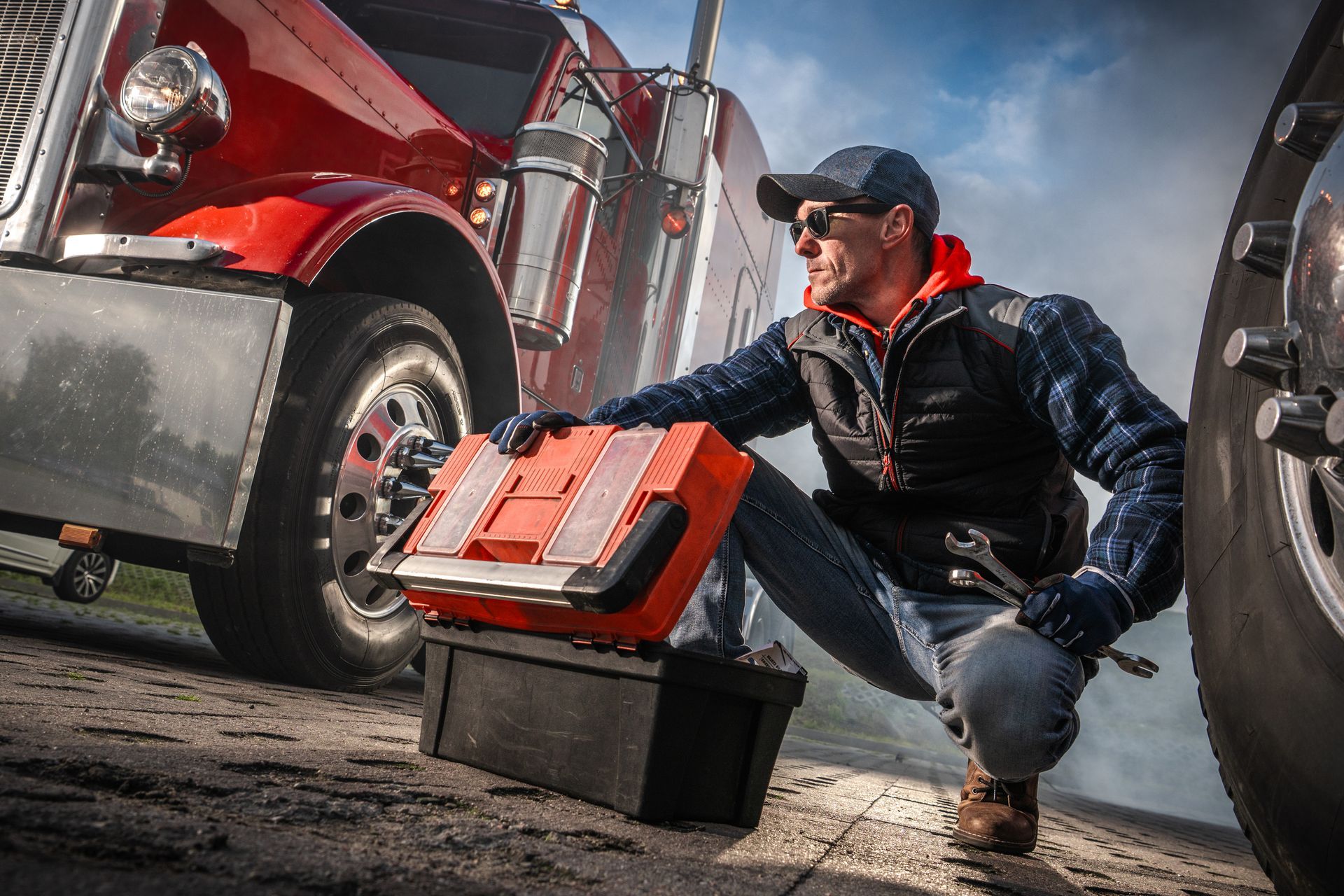 Mechanic kneeling by a red truck, pulling a red toolbox from under the vehicle
