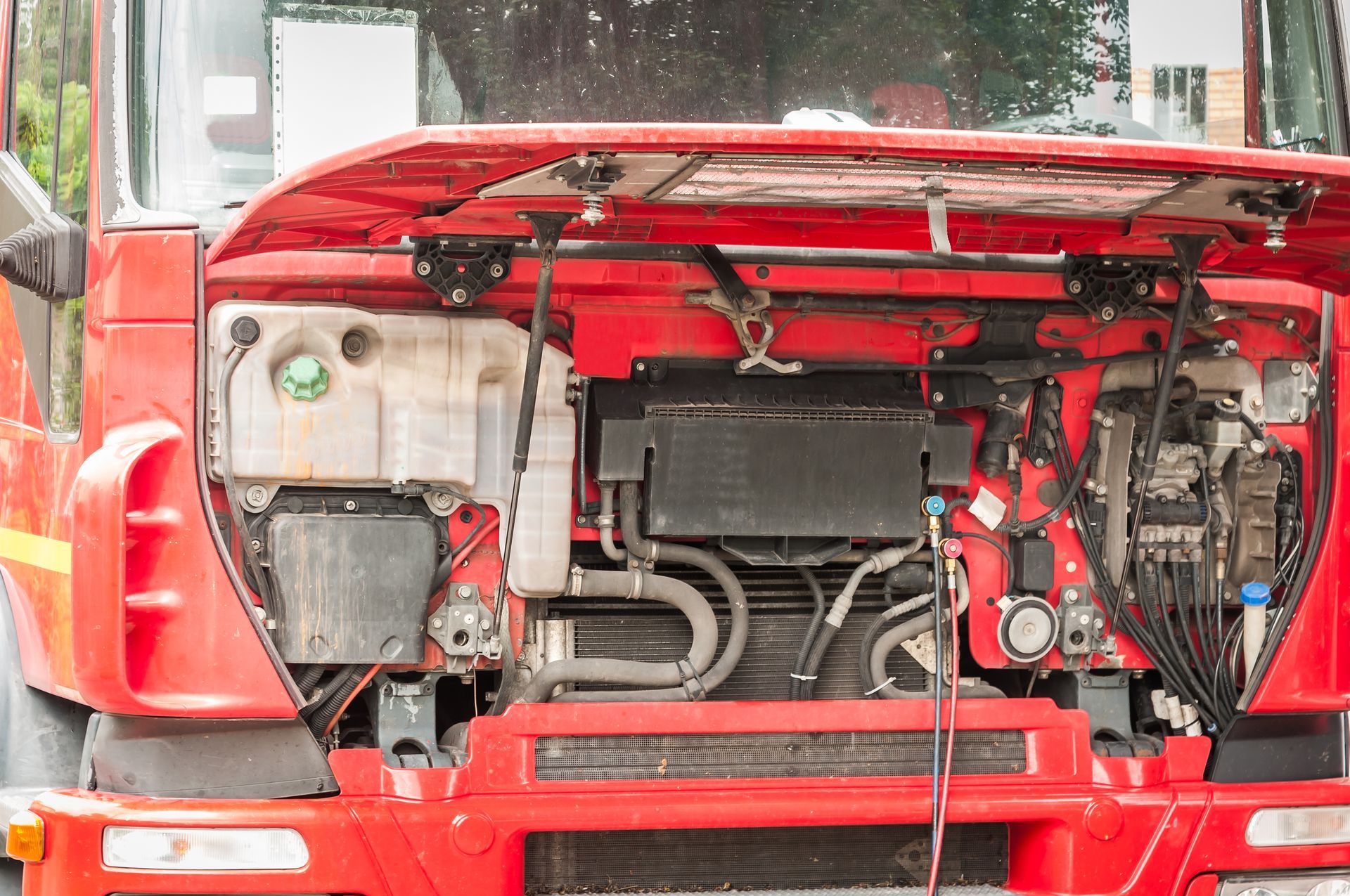 Open red truck engine compartment with the hood raised, exposing mechanical parts and wiring.
