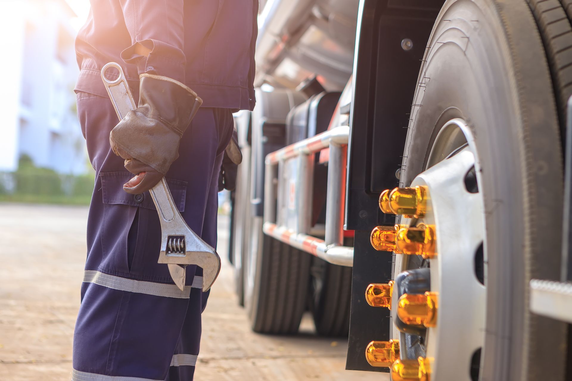 Worker in safety vest standing beside a truck wheel and reflective cone markers on a sunny street