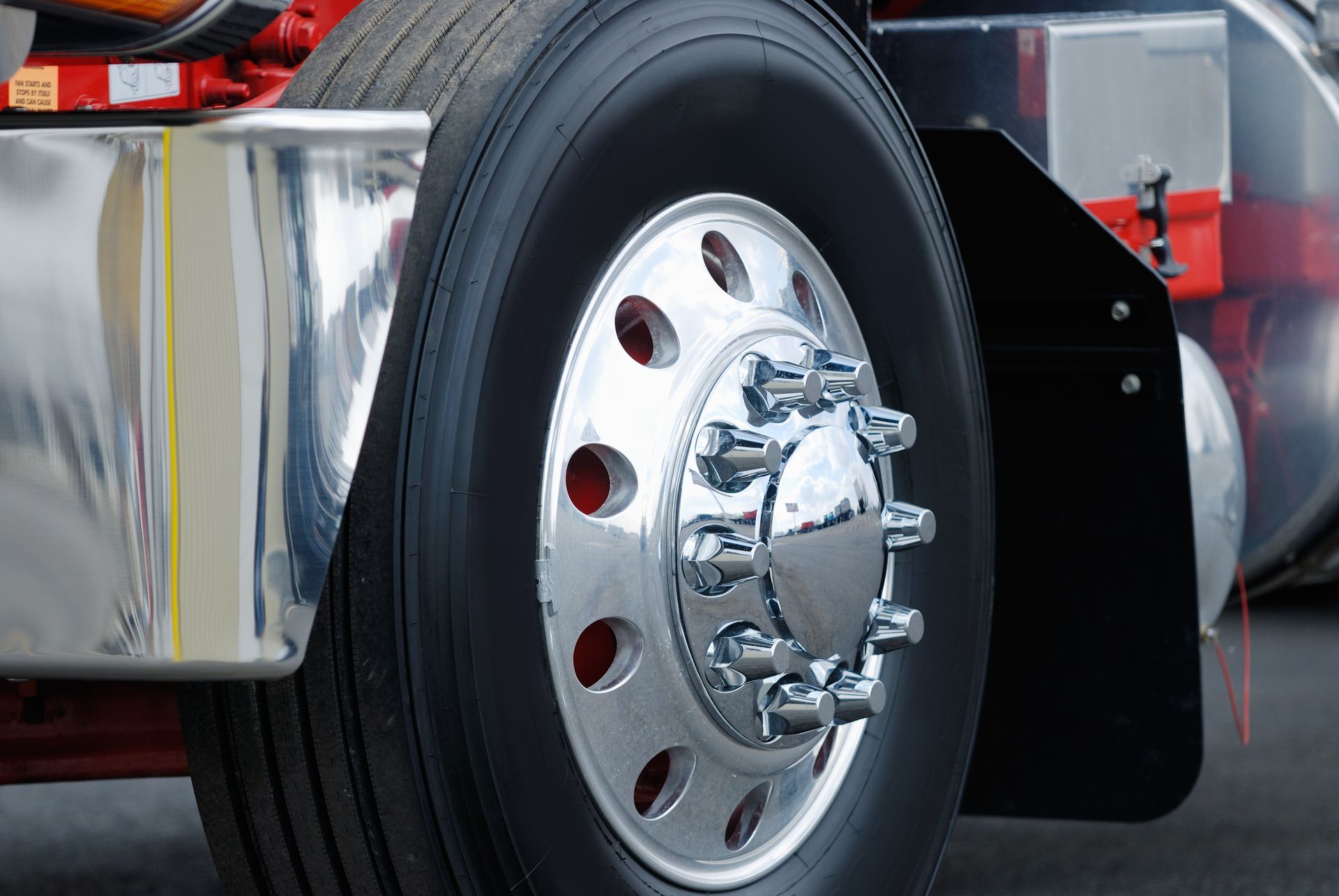 Close-up of a chrome truck wheel with a black tire and red vehicle body in the background