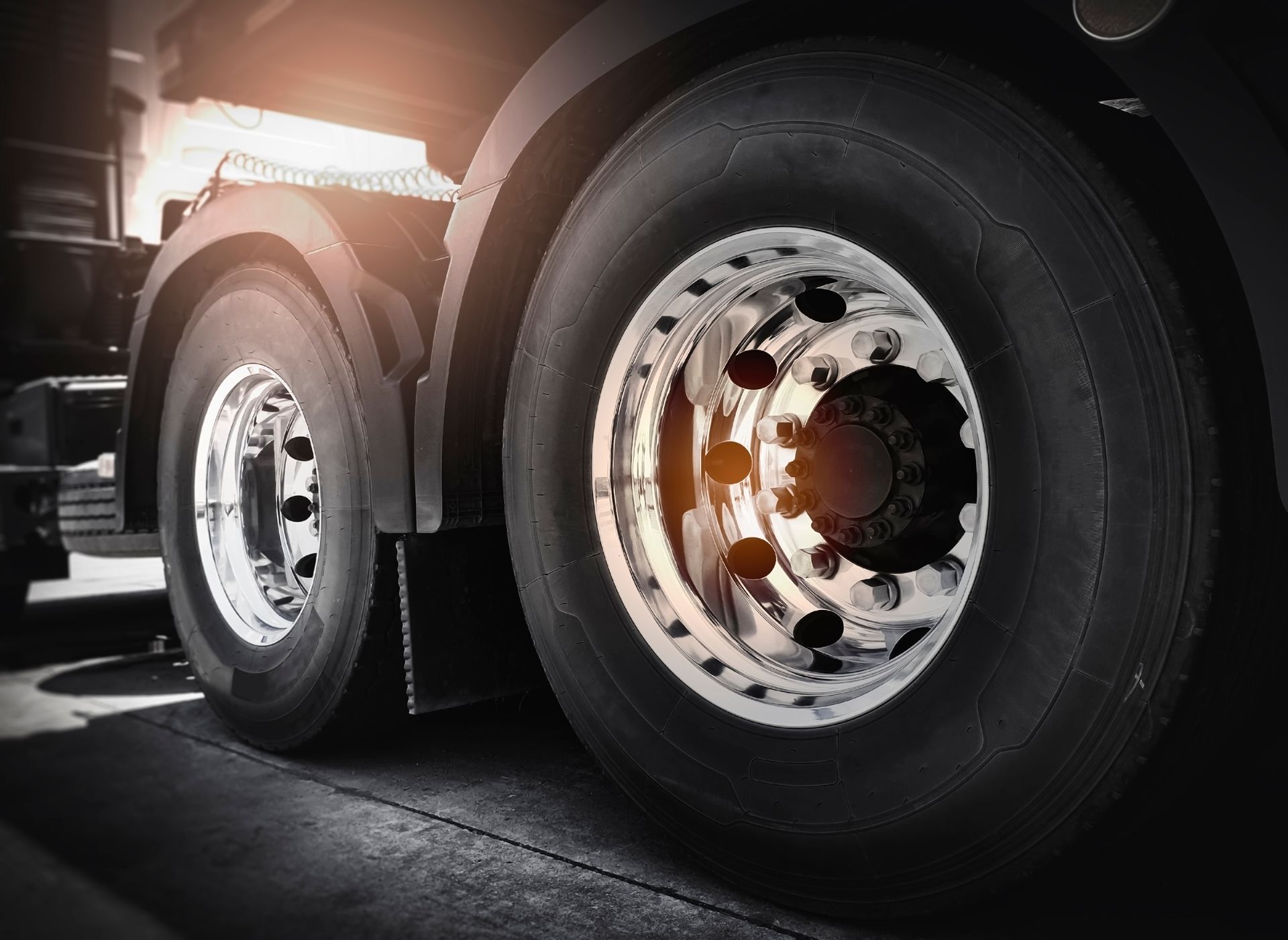 Close-up of truck wheels with chrome rims on a paved road at sunset