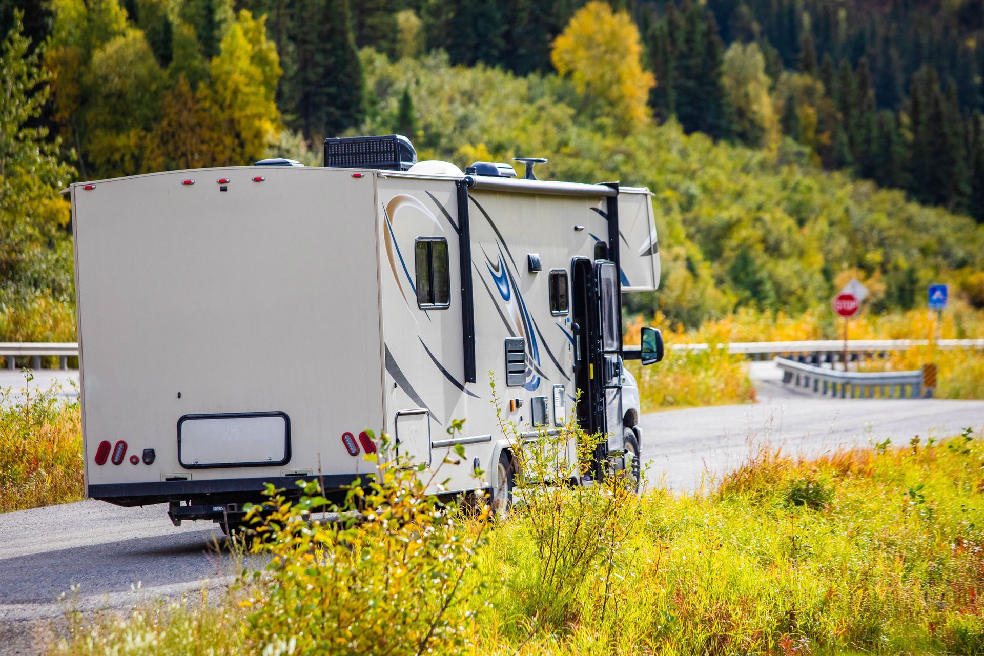 White RV parked on a roadside beside yellow wildflowers, with autumn trees in the background