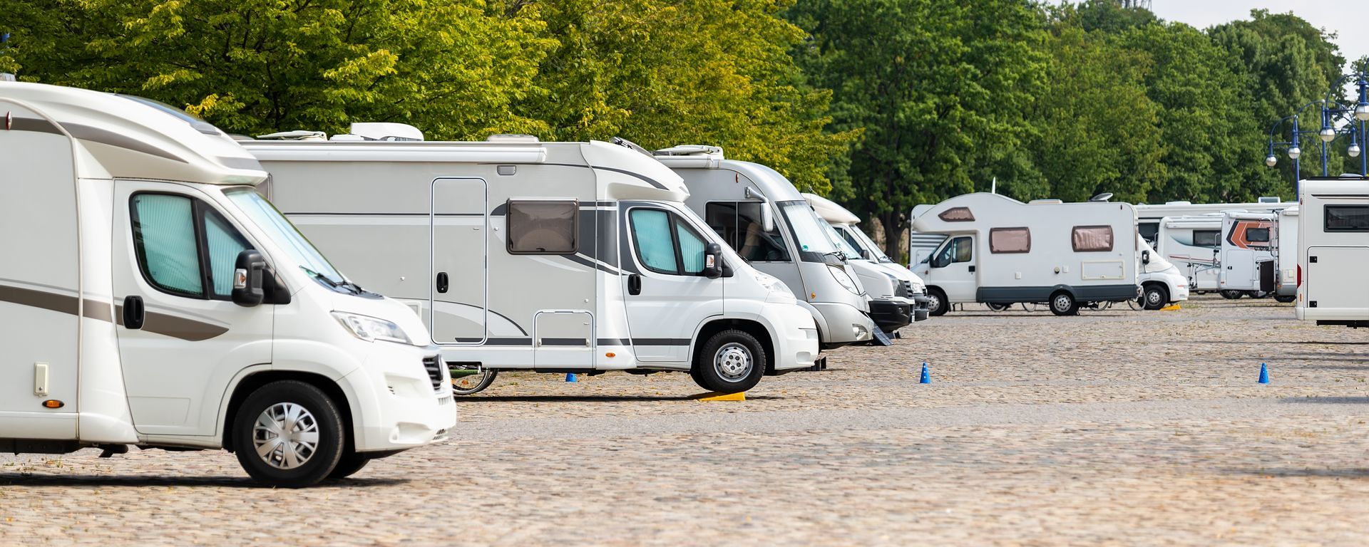 White camper vans parked on a gravel lot beside green trees under a clear sky