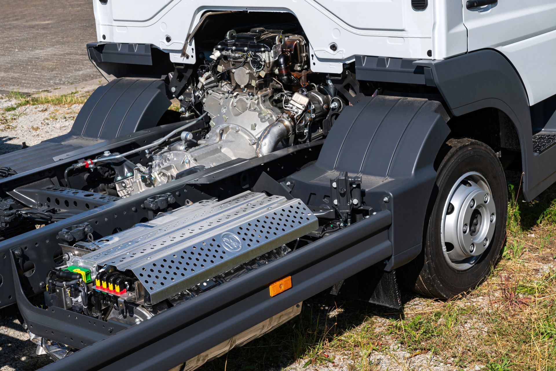 White truck chassis cab with exposed engine and rear battery pack on a grassy roadside
