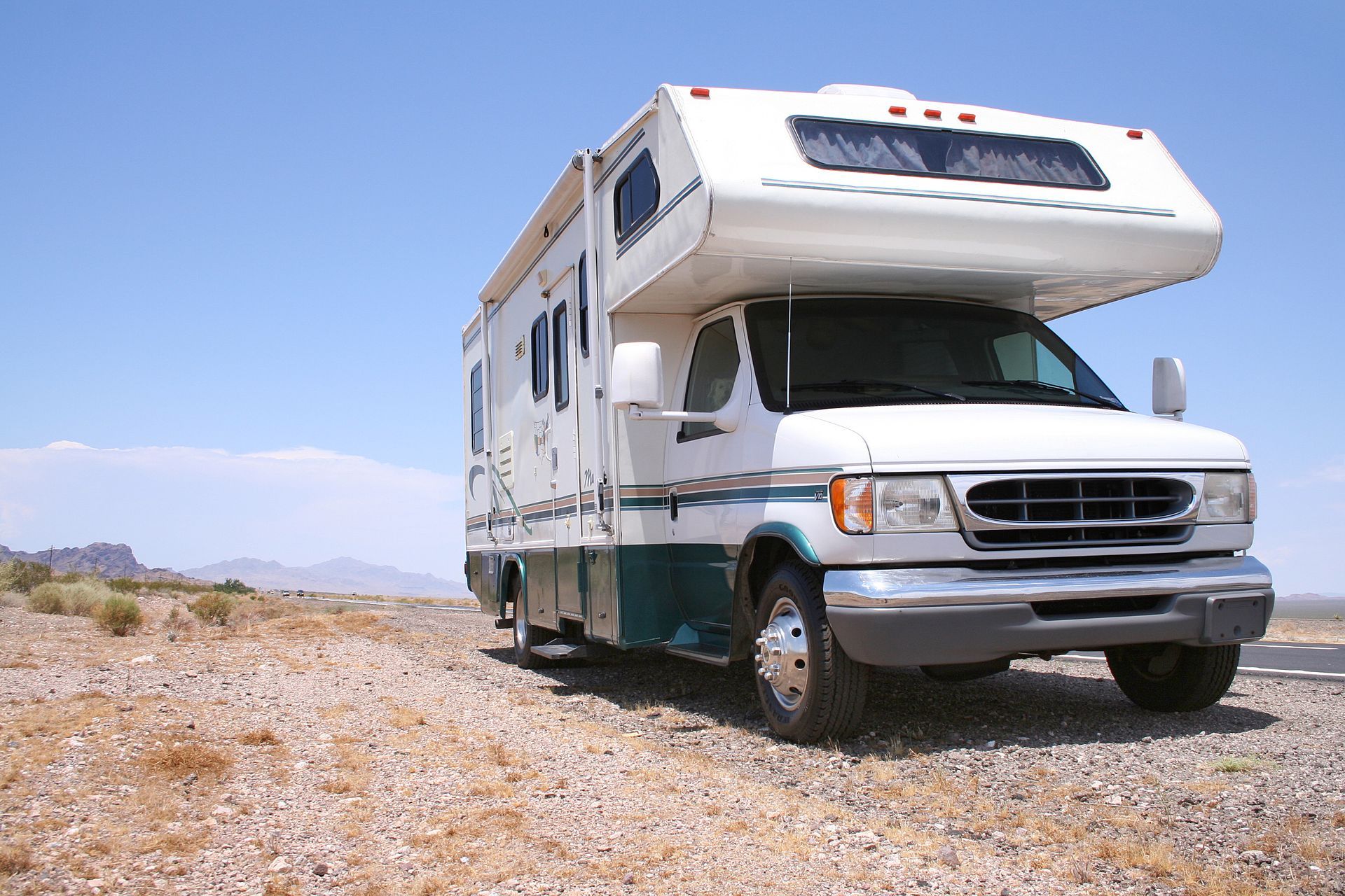 White and green RV parked on a rocky desert road under a clear sky