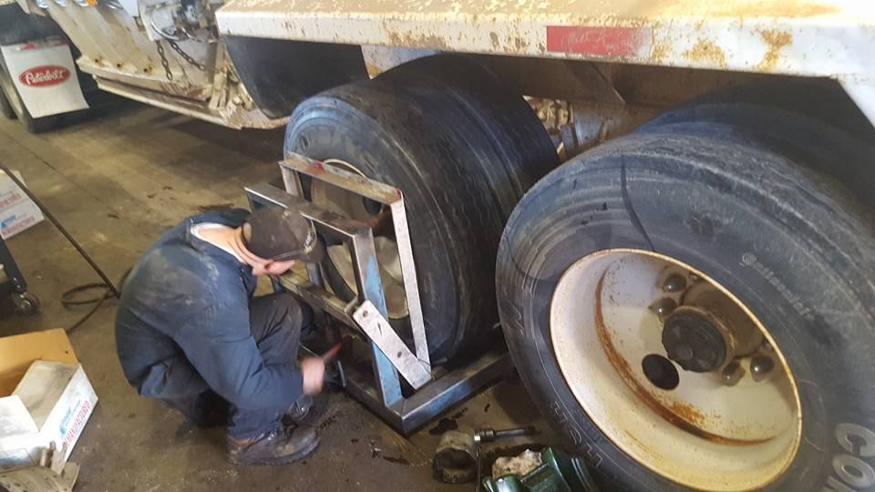 Mechanic working under a truck near dual rear wheels in a repair shop