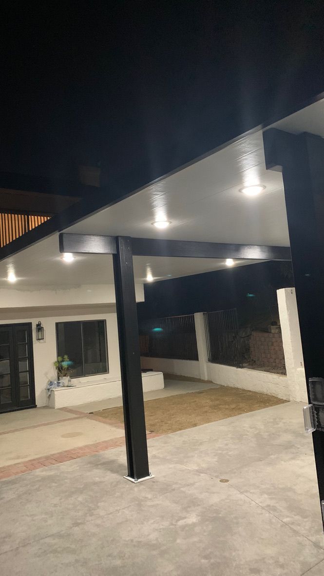 Covered outdoor patio with black columns, white ceiling, and lights at night