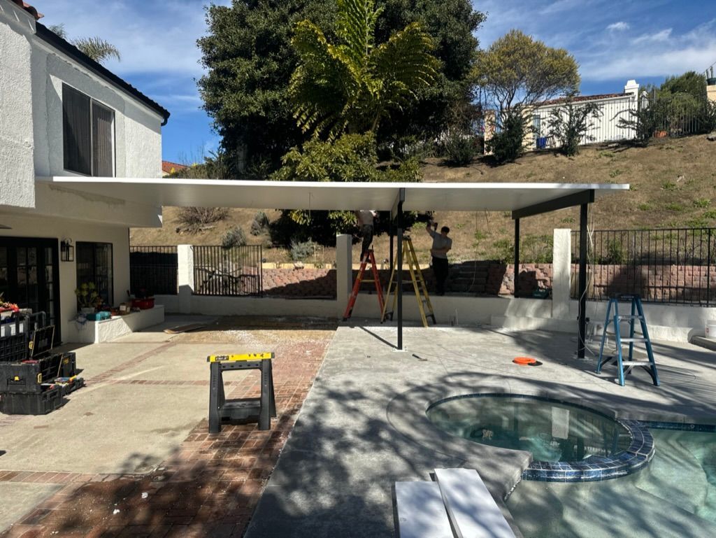 Backyard patio with a pool, covered seating area, and trees on a sunny day