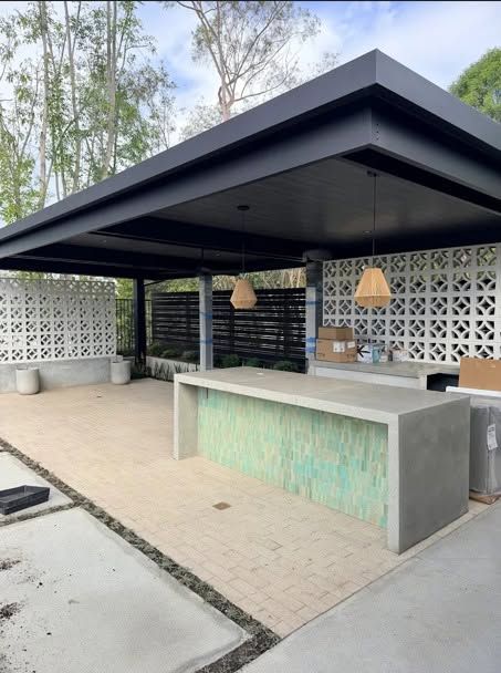 Outdoor bar pavilion with dark roof, concrete counter, and white patterned wall panels