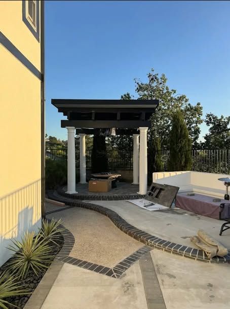 Patio with curved concrete walkway, pergola seating area, and yellow building exterior in bright daylight