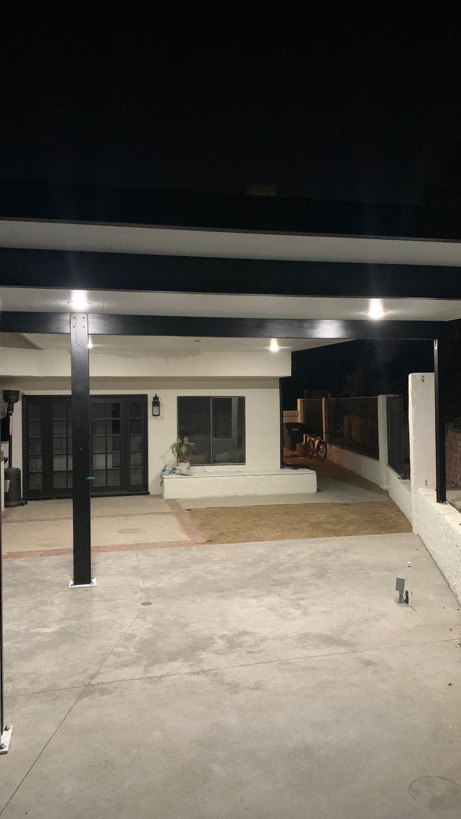 Nighttime view of a covered front porch with concrete driveway, white walls, and black support columns
