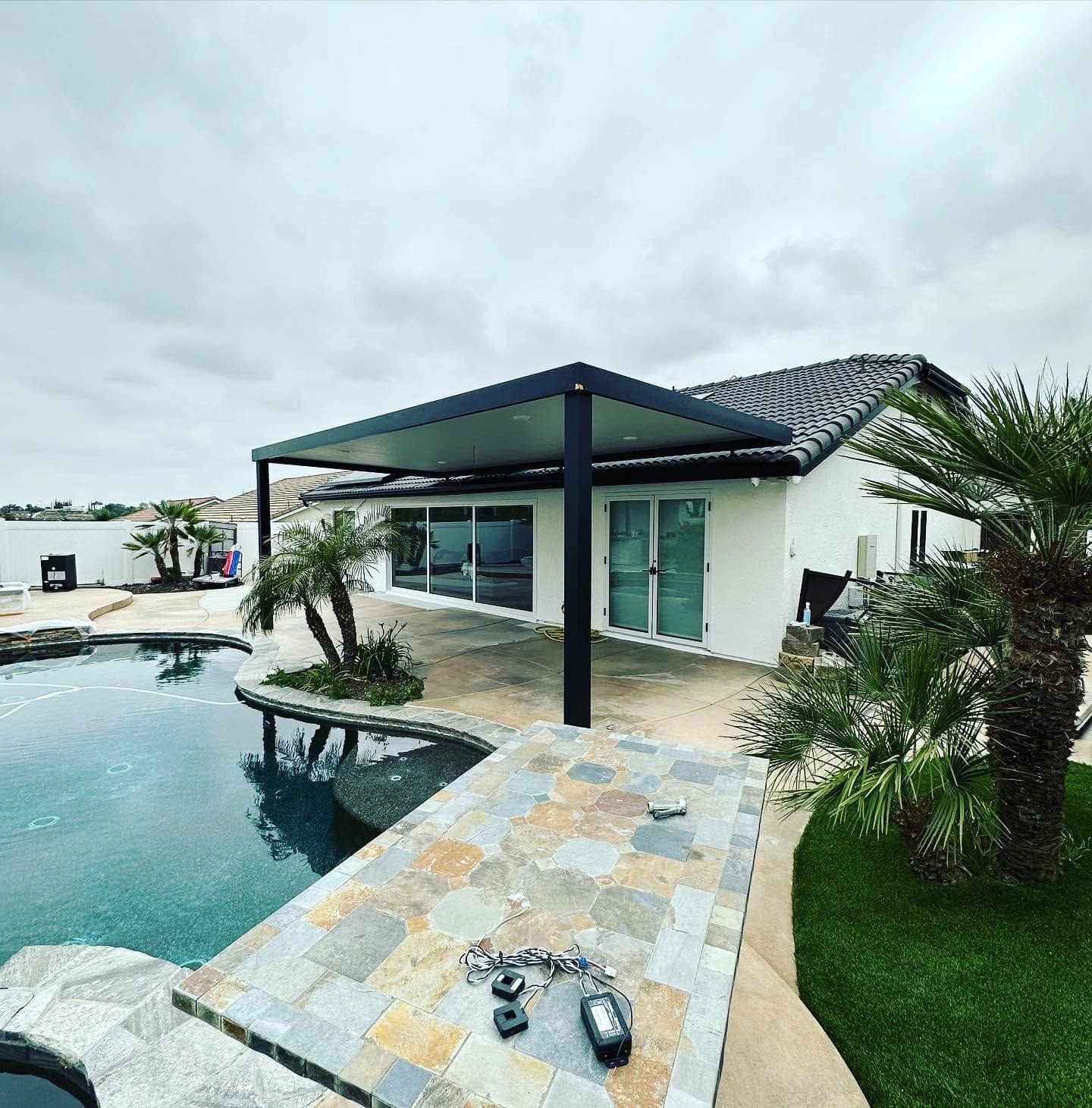 Modern white villa with covered patio and turquoise pool beside a tiled deck and palm landscaping