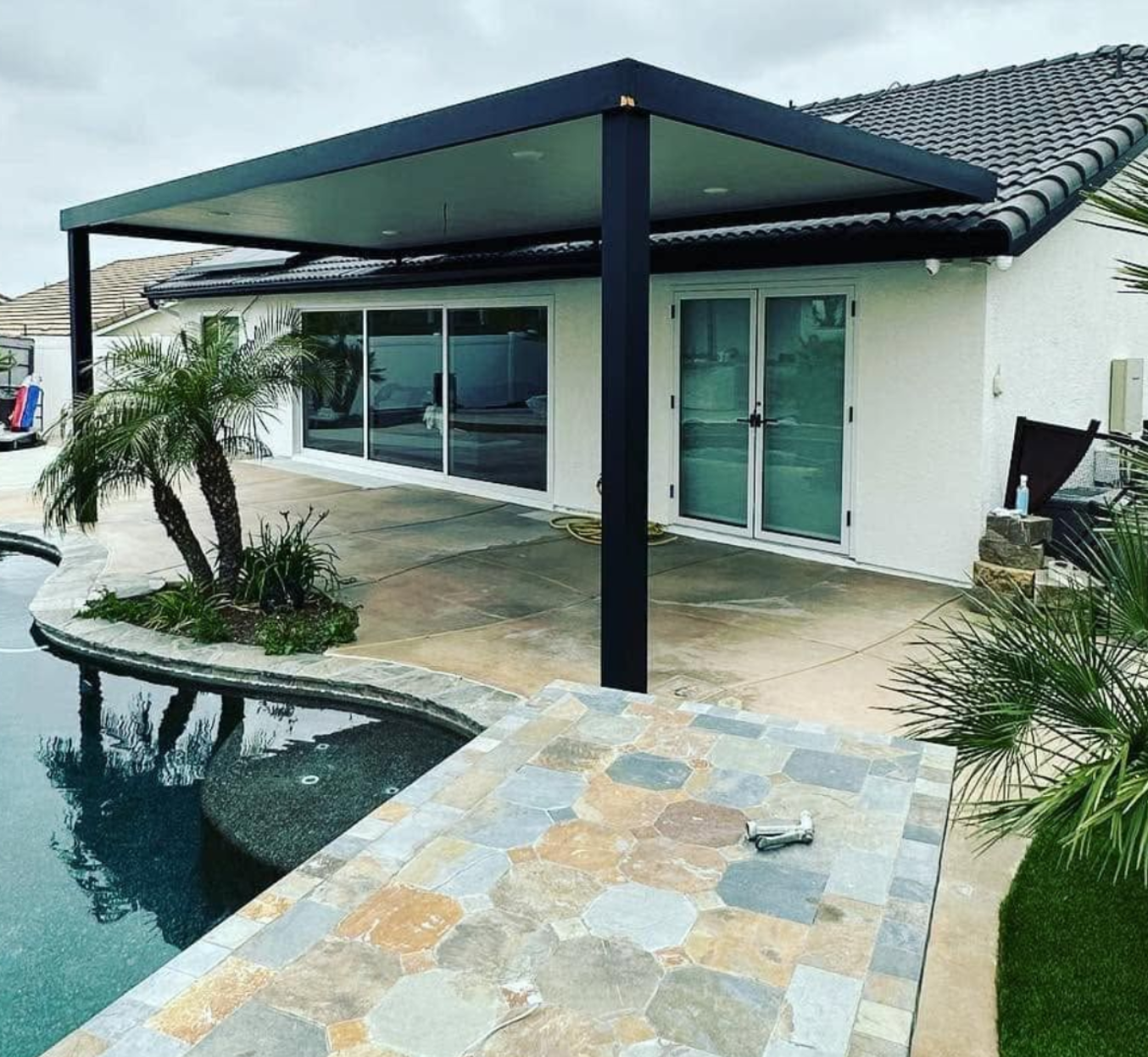Modern house patio with covered seating area, pool, and stone walkway