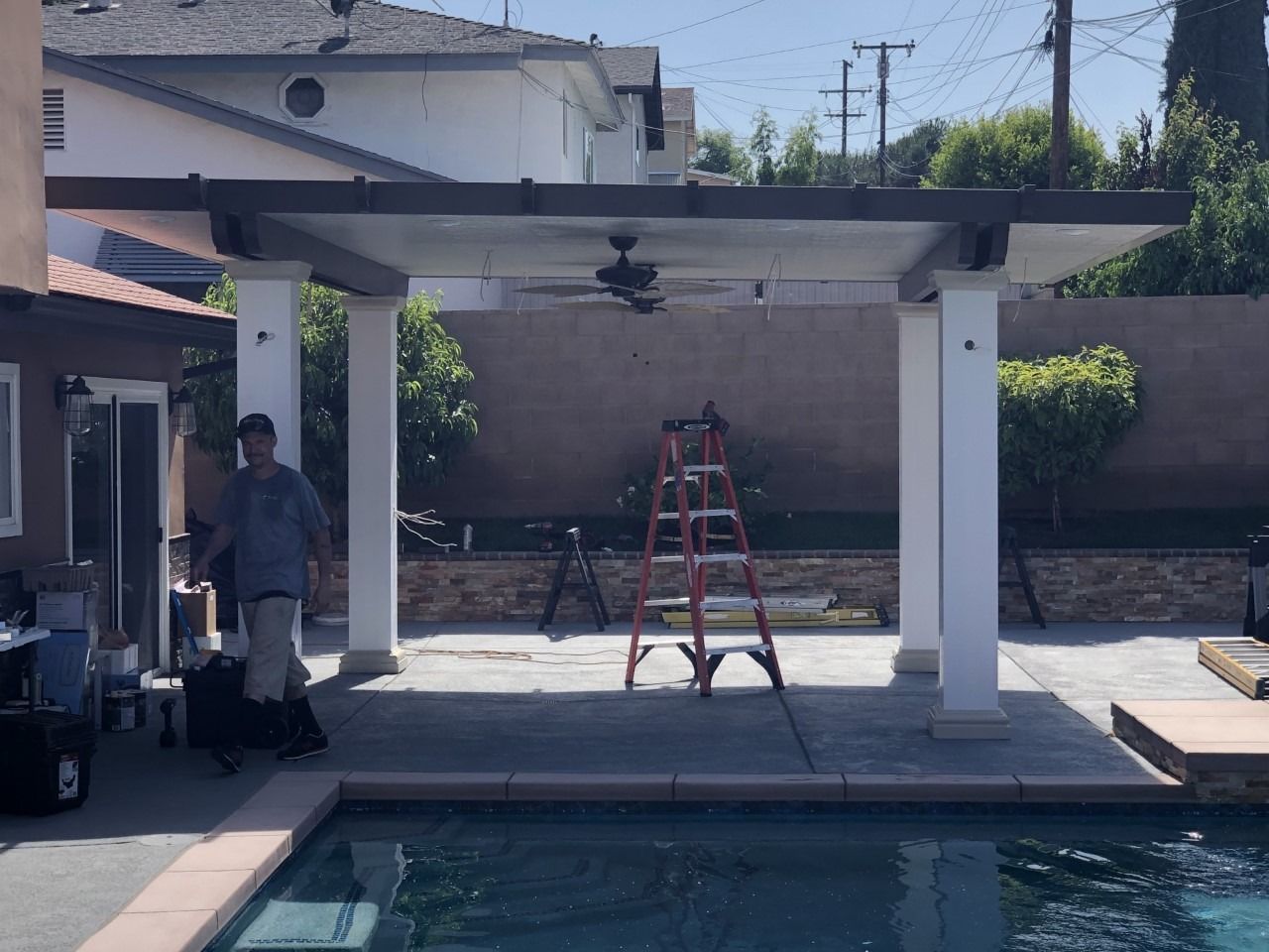 Backyard patio with pergola, ladder, and a person standing by a pool