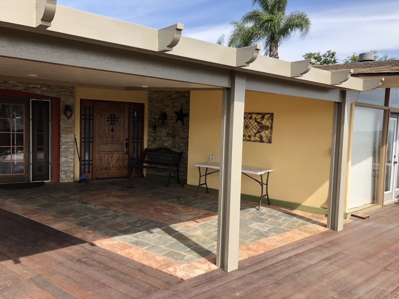 Covered patio with tiled floor, beige columns, and glass doors opening to a house exterior.