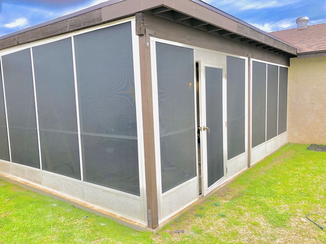 Screened patio enclosure with gray mesh panels and white-framed doors beside a house on grass