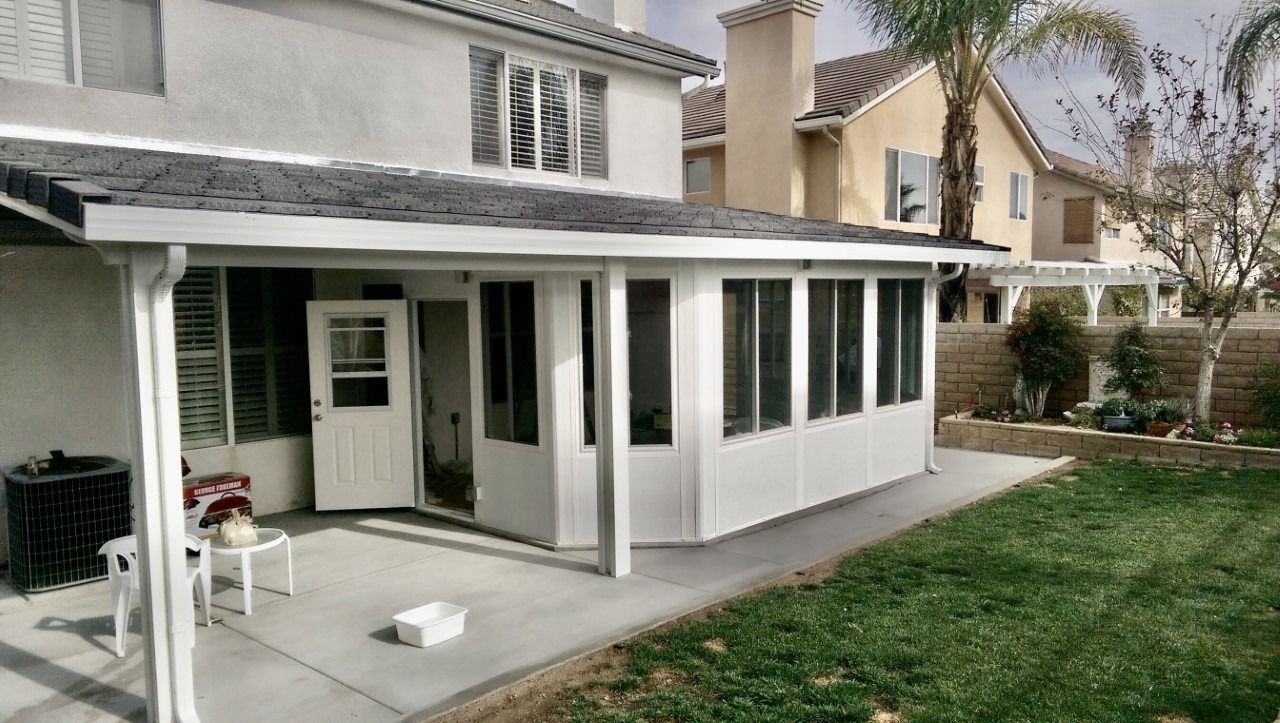 Backyard patio attached to a house with white screened porch and gray siding, beside a green lawn.