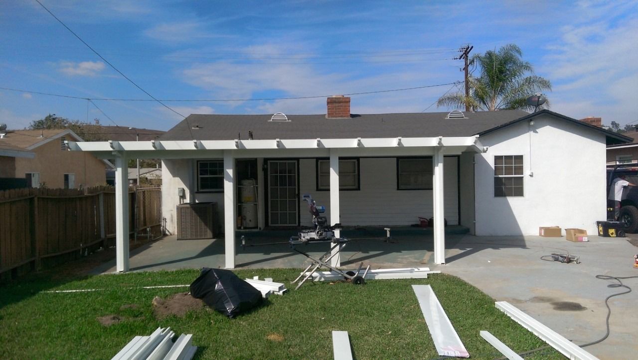 Backyard patio under construction with white pergola posts, scattered materials, and a grassy lawn