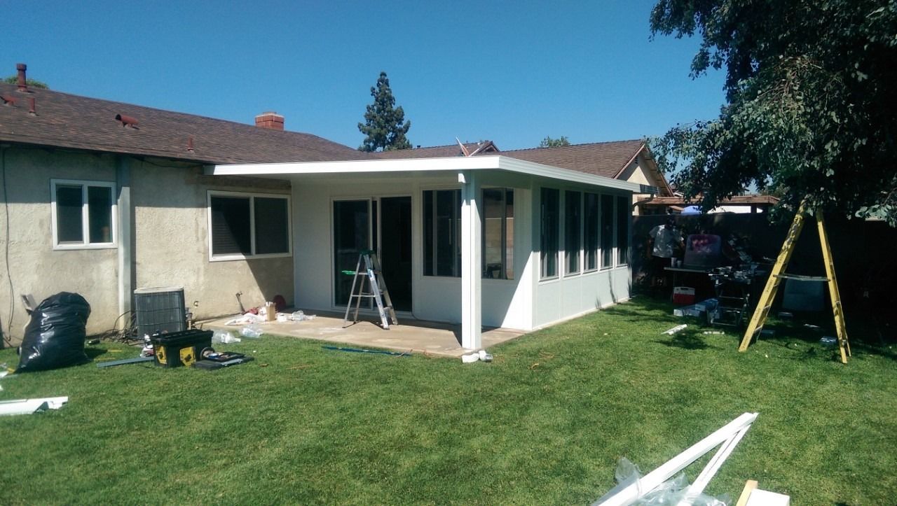 Backyard with a beige house, covered patio, ladder, and swing set on a sunny day
