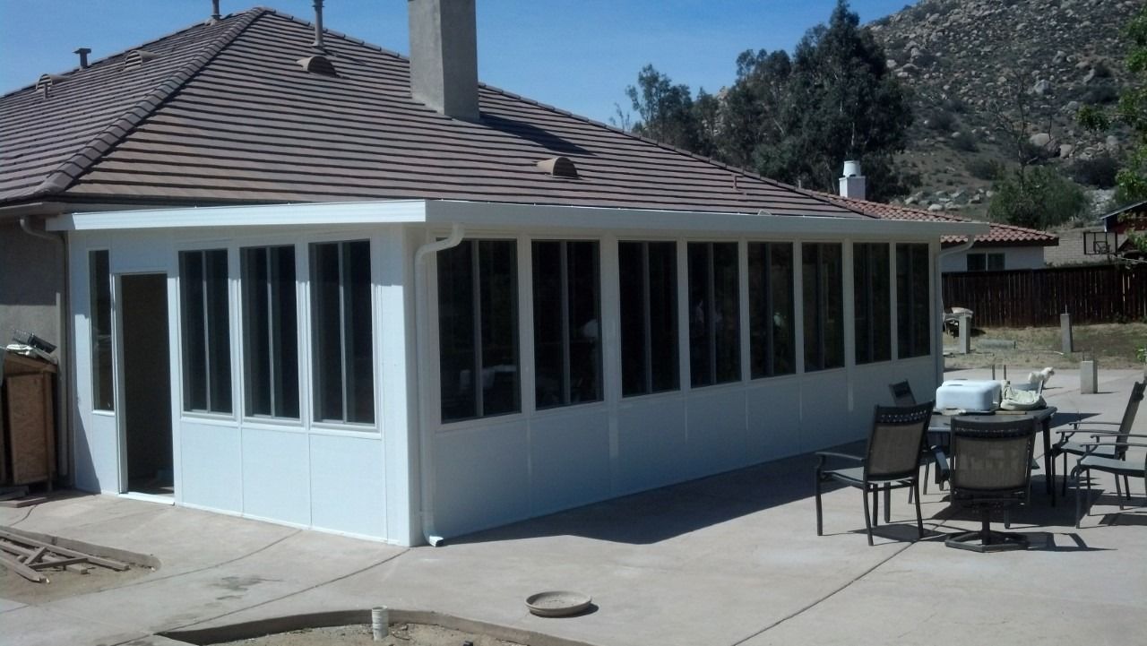 White sunroom addition with many windows beside a patio and outdoor table under a tiled roof.
