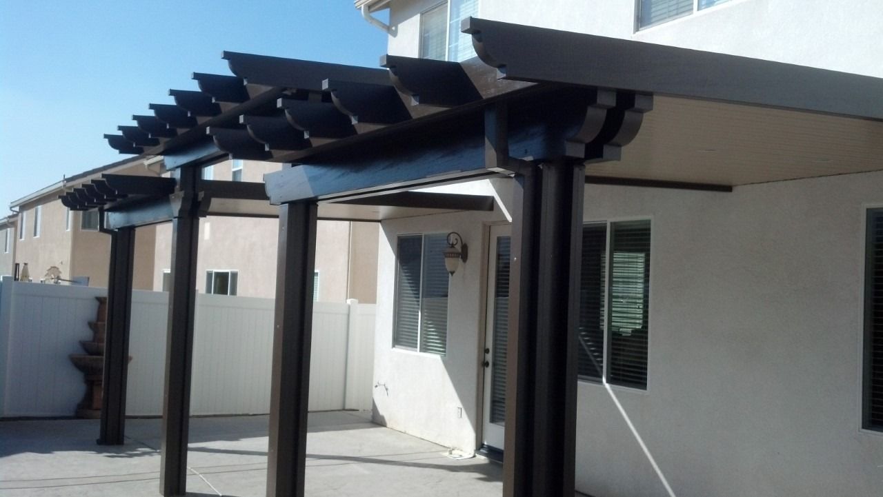 Modern house patio with dark pergola beams and white exterior walls in bright sunlight