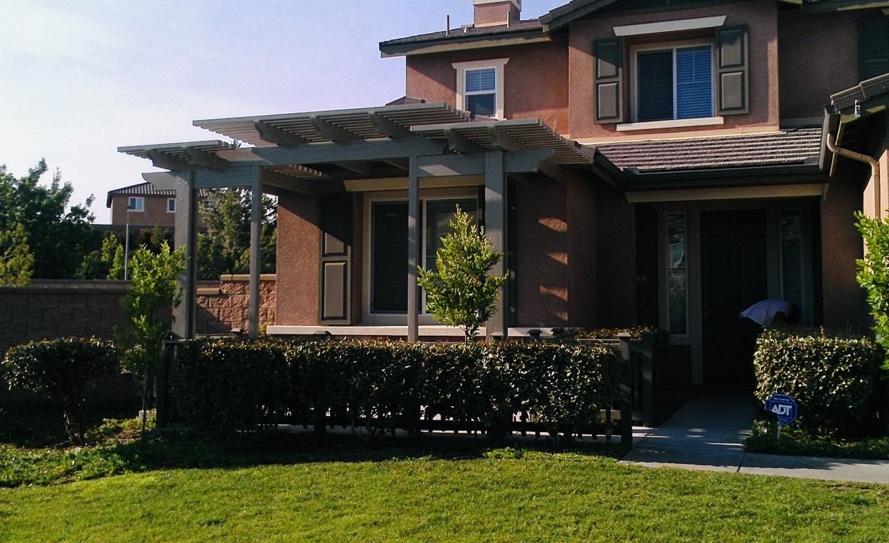Two-story brick house with a covered porch, black fence, and green lawn in bright sunlight