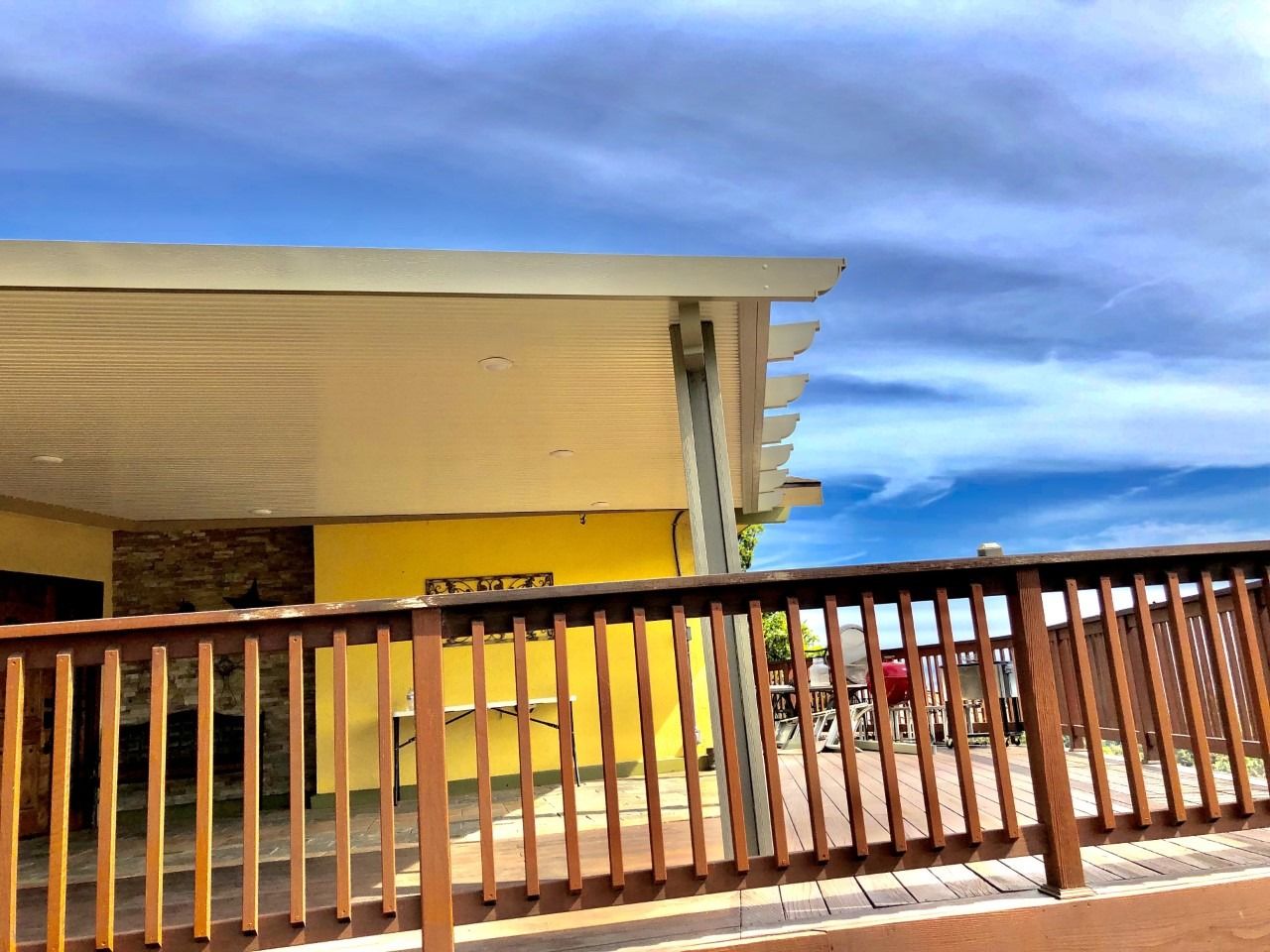 Wooden deck railing in front of a yellow building under a cloudy sky