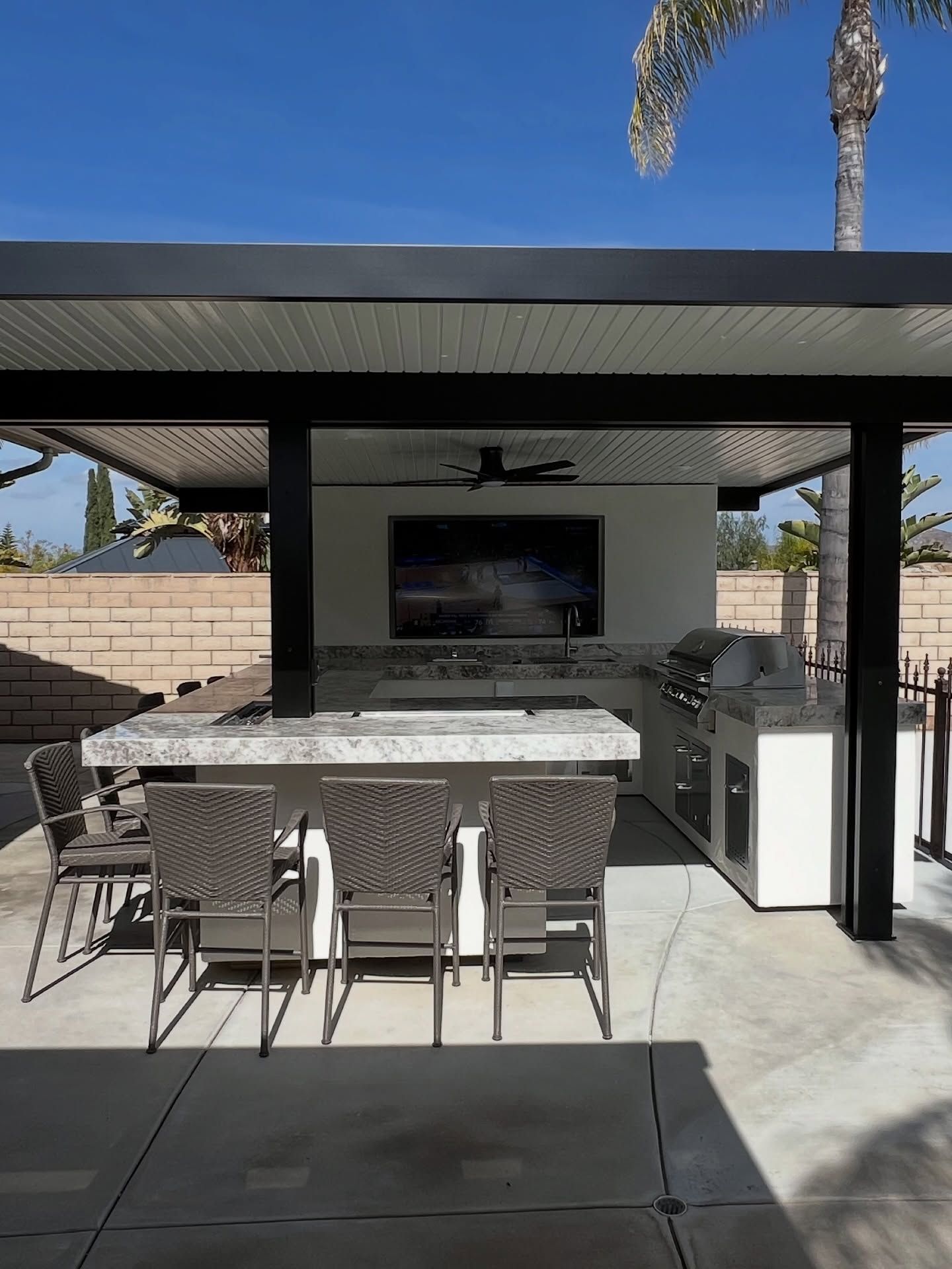 Modern outdoor patio with kitchen grill, dining table, and bar stools under a covered pergola.