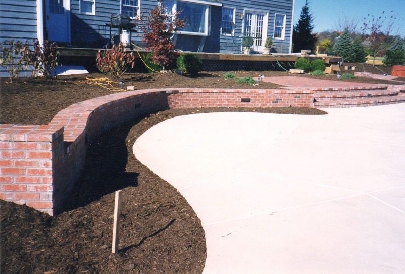 Curved brick retaining wall beside a concrete patio in front of a blue house