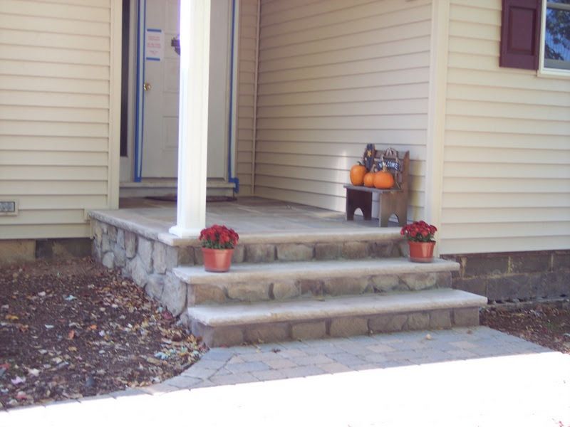 Front porch with steps, potted flowers, and a small pumpkin display beside a beige house