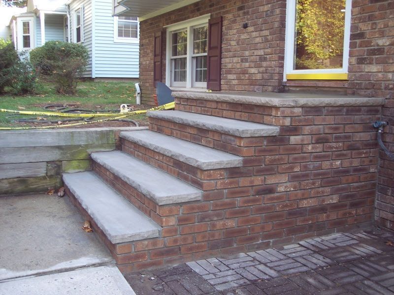 Brick front steps leading to a house entrance with a small concrete walkway and garden bed