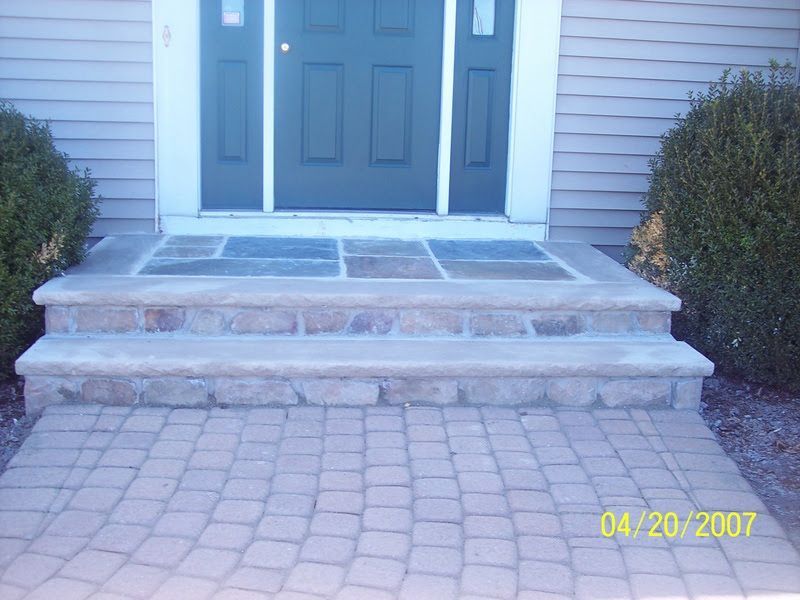 Front entry with stone steps, paver walkway, and blue double doors