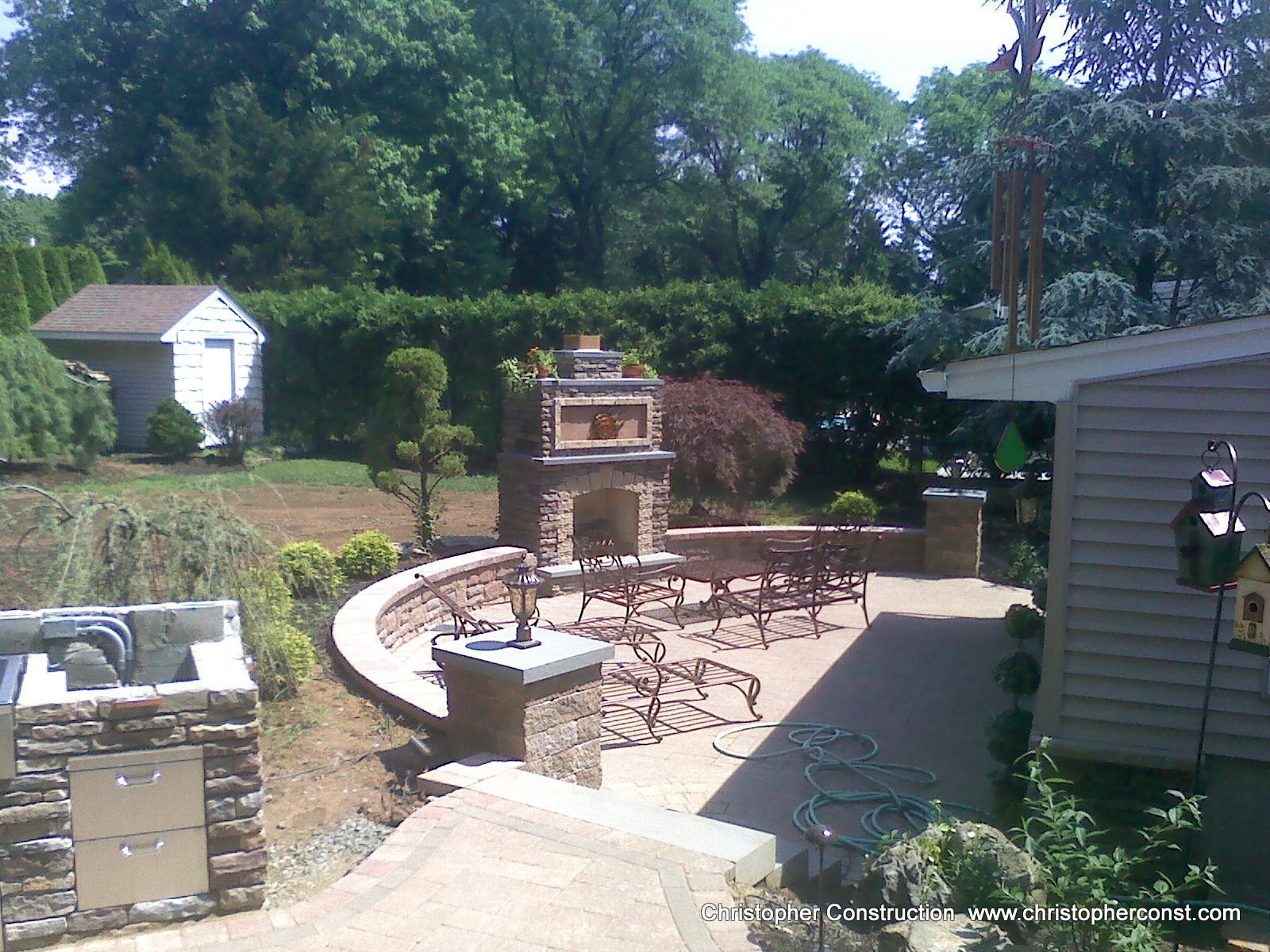 Backyard patio with stone fire pit, curved bench, and outdoor seating under trees