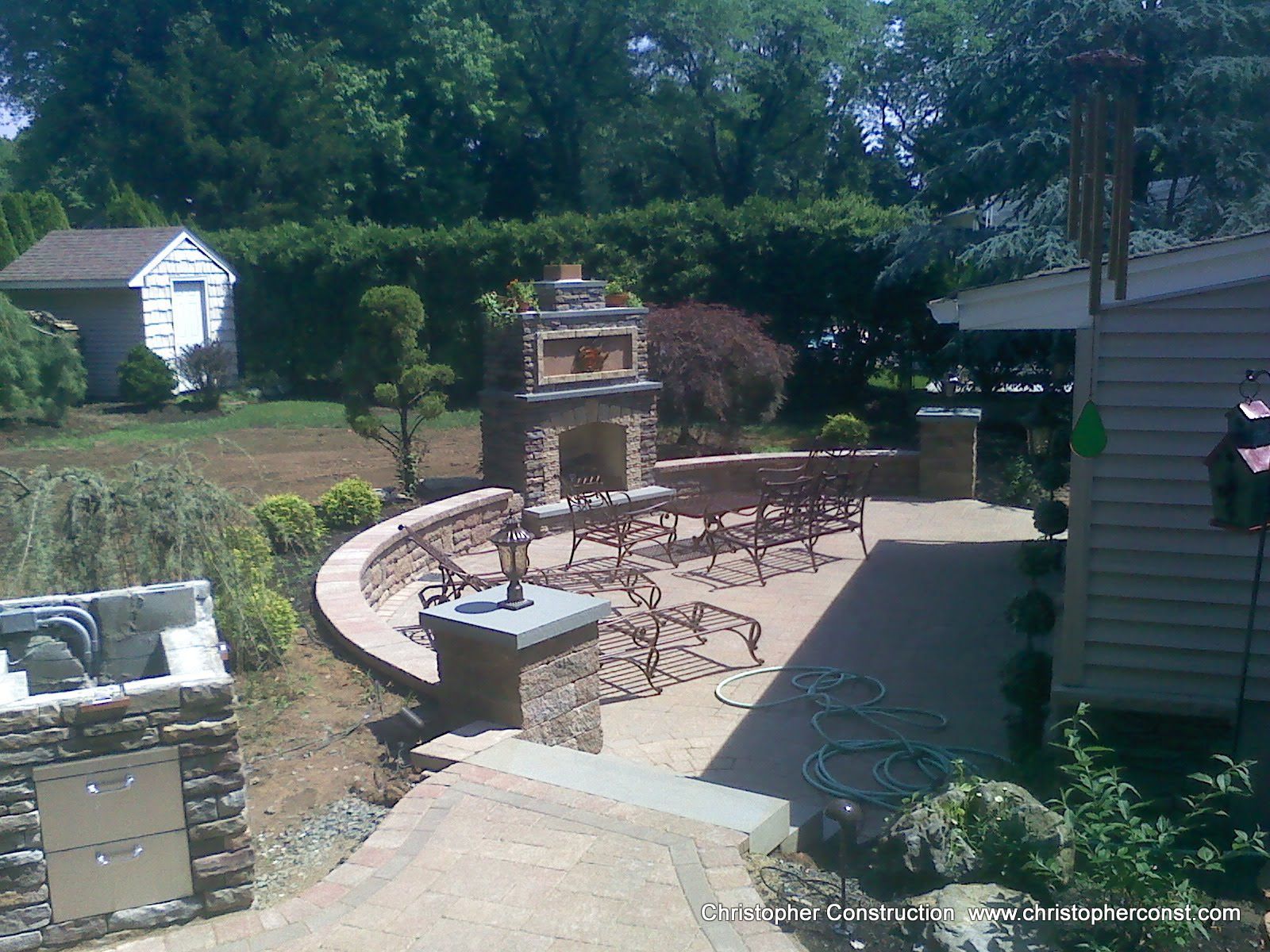 Backyard patio with stone fire pit, outdoor dining table, and brick grill under trees