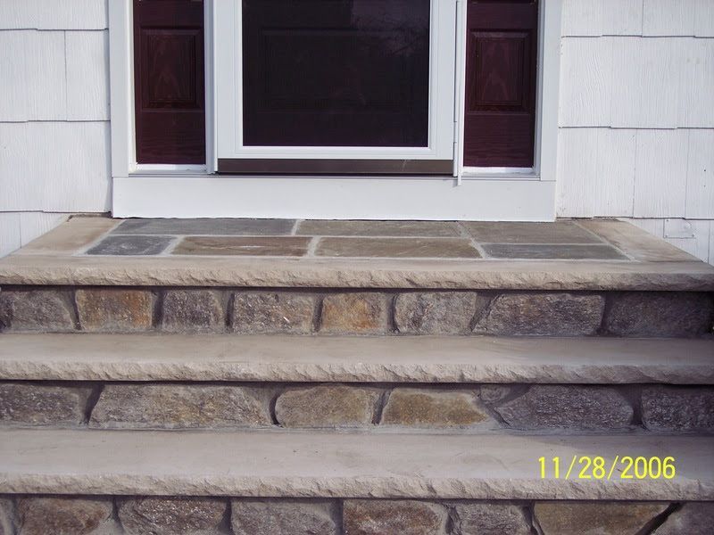 Front steps of a house with stone risers leading to a white door and windows