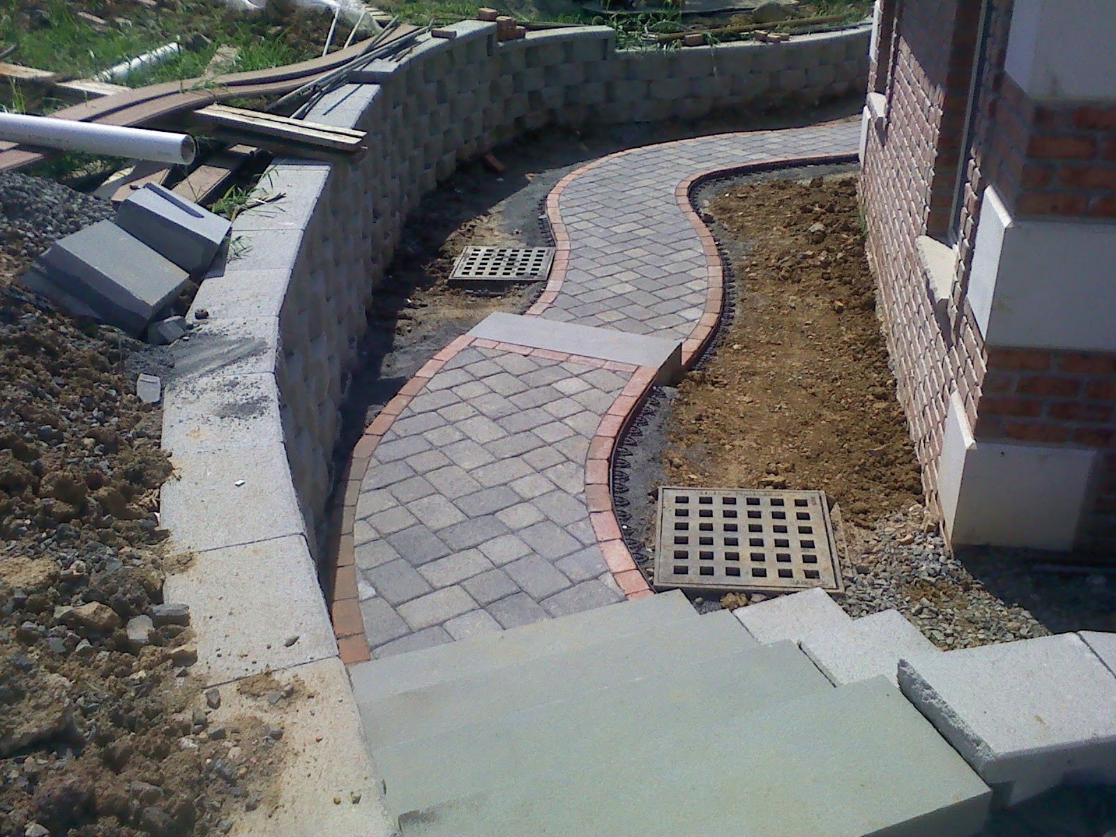 Curved brick garden path beside a house, bordered by low stone walls and dry landscaping.