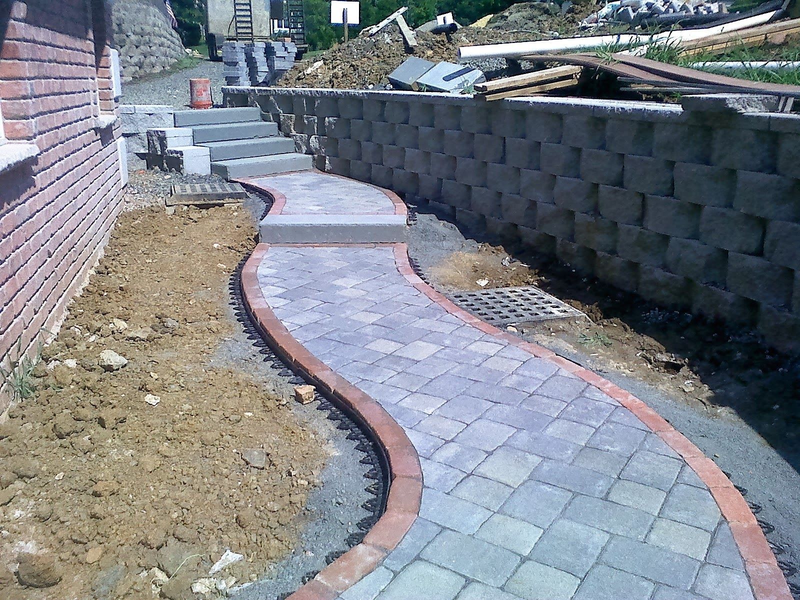 Curving stone walkway under construction beside a brick wall and retaining wall