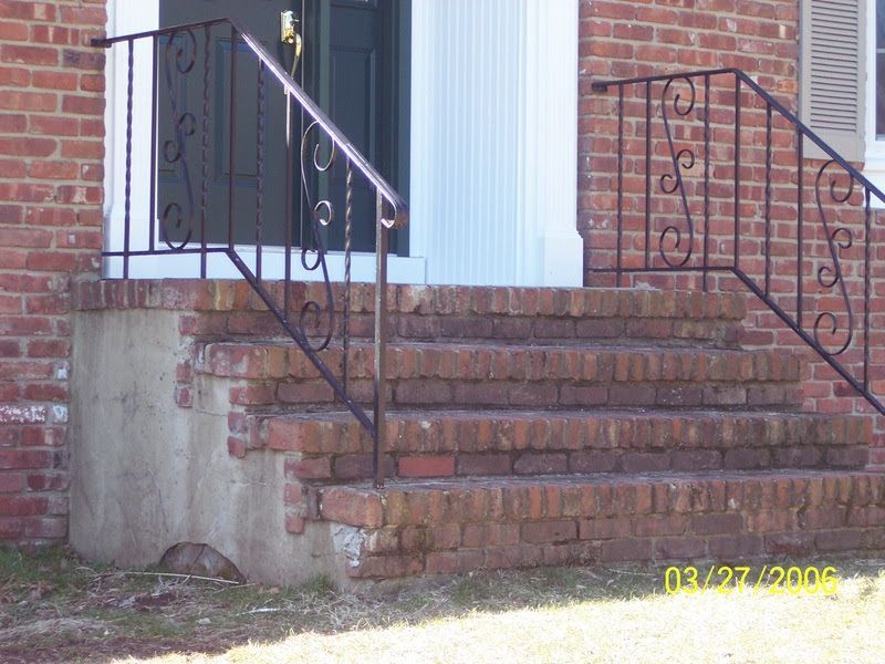 Brick front steps with black wrought-iron railings beside a house entrance.